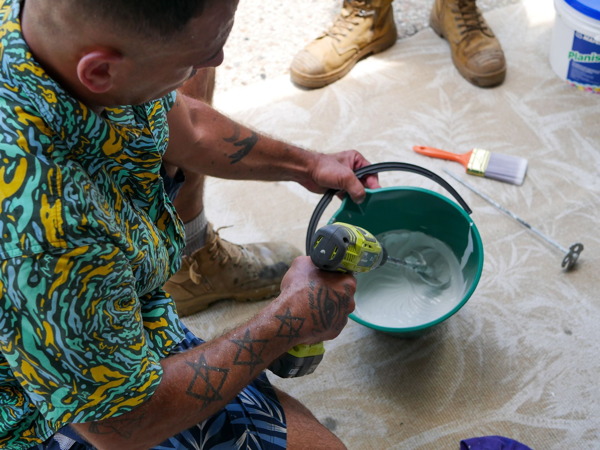 A man is holding a drill next to a bucket of liquid
