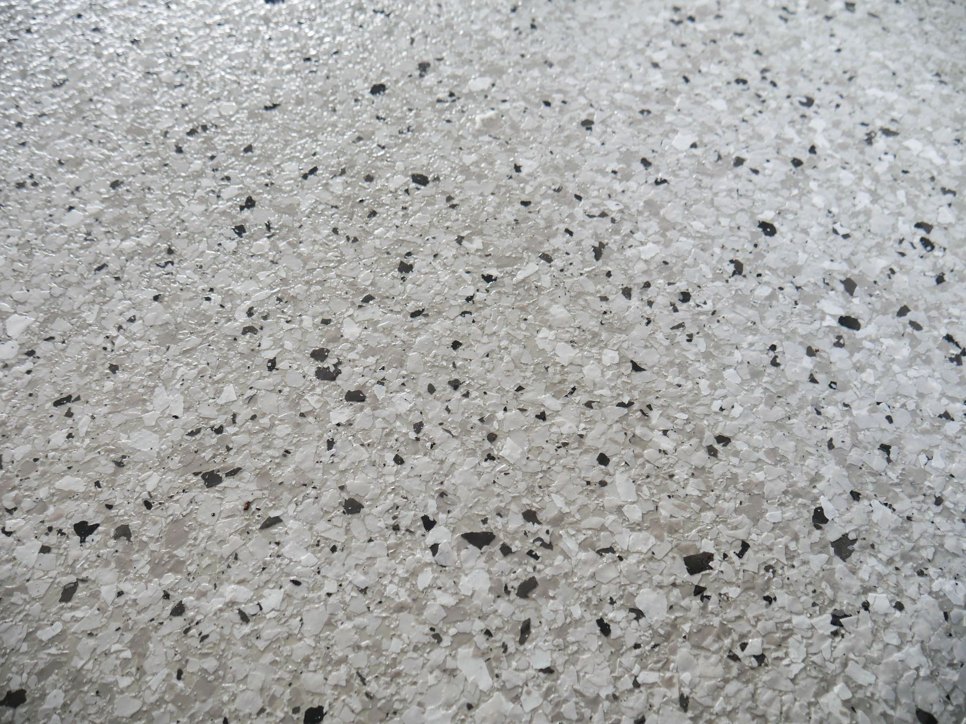 A close-up of a completed epoxy driveway with a white floor with black spots.