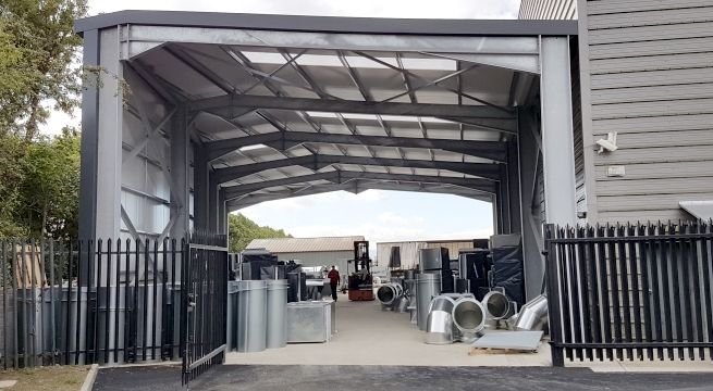 outside view of steel frame of 45,000 sq. ft. expanded manufacturing floor area with large metal ducts and black steel fence