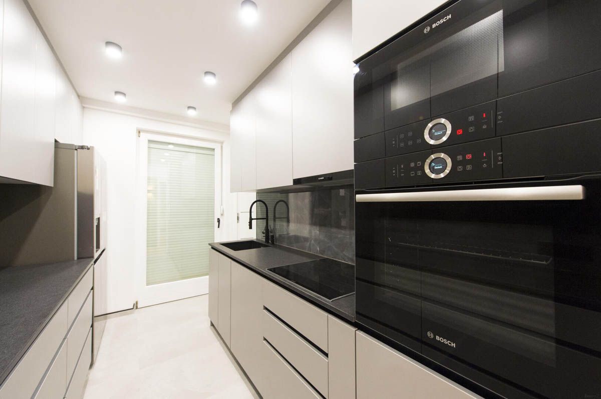 Moderne Küche mit schwarzen Geräten, hellgrauen Schränken und dunklen Arbeitsplatten.