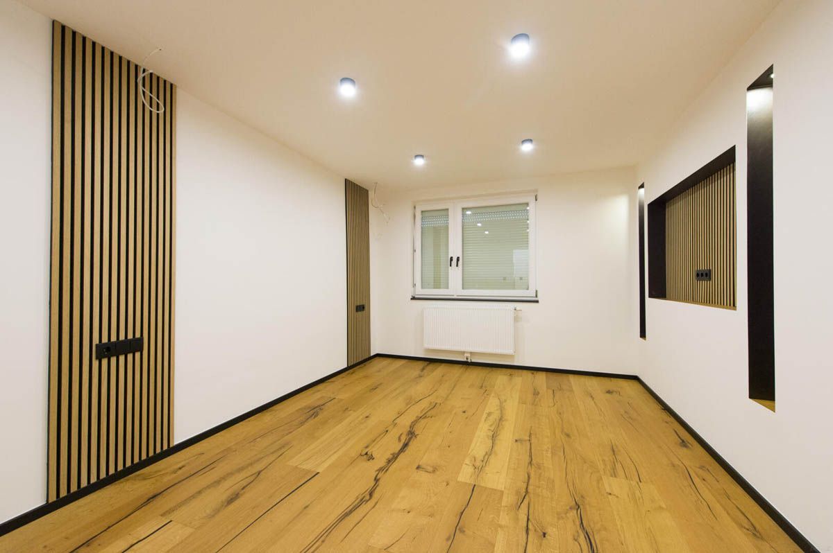 Leerer Raum mit Holzboden und getäfelter Wand, weißen Wänden und eingelassenen Deckenleuchten.
