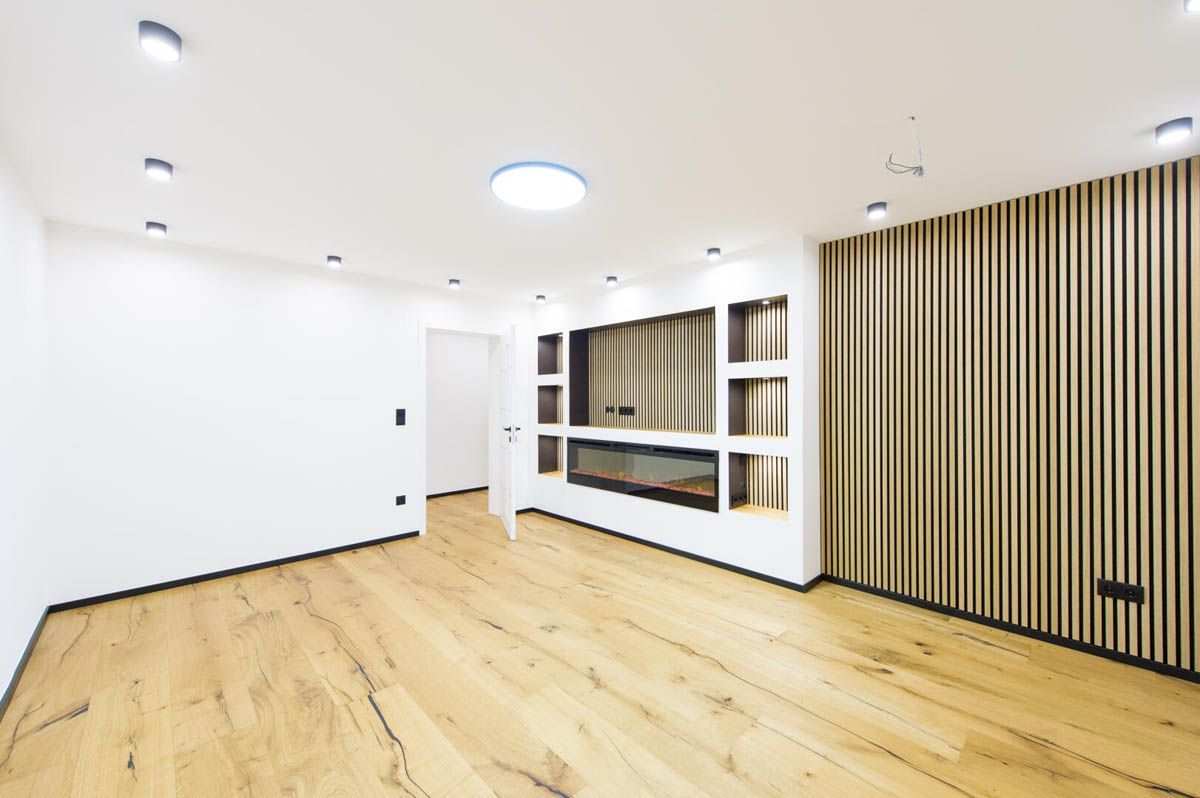 Leeres, modernes Wohnzimmer mit Holzböden, Einbauleuchten und einer dekorativen Akzentwand aus Holz.