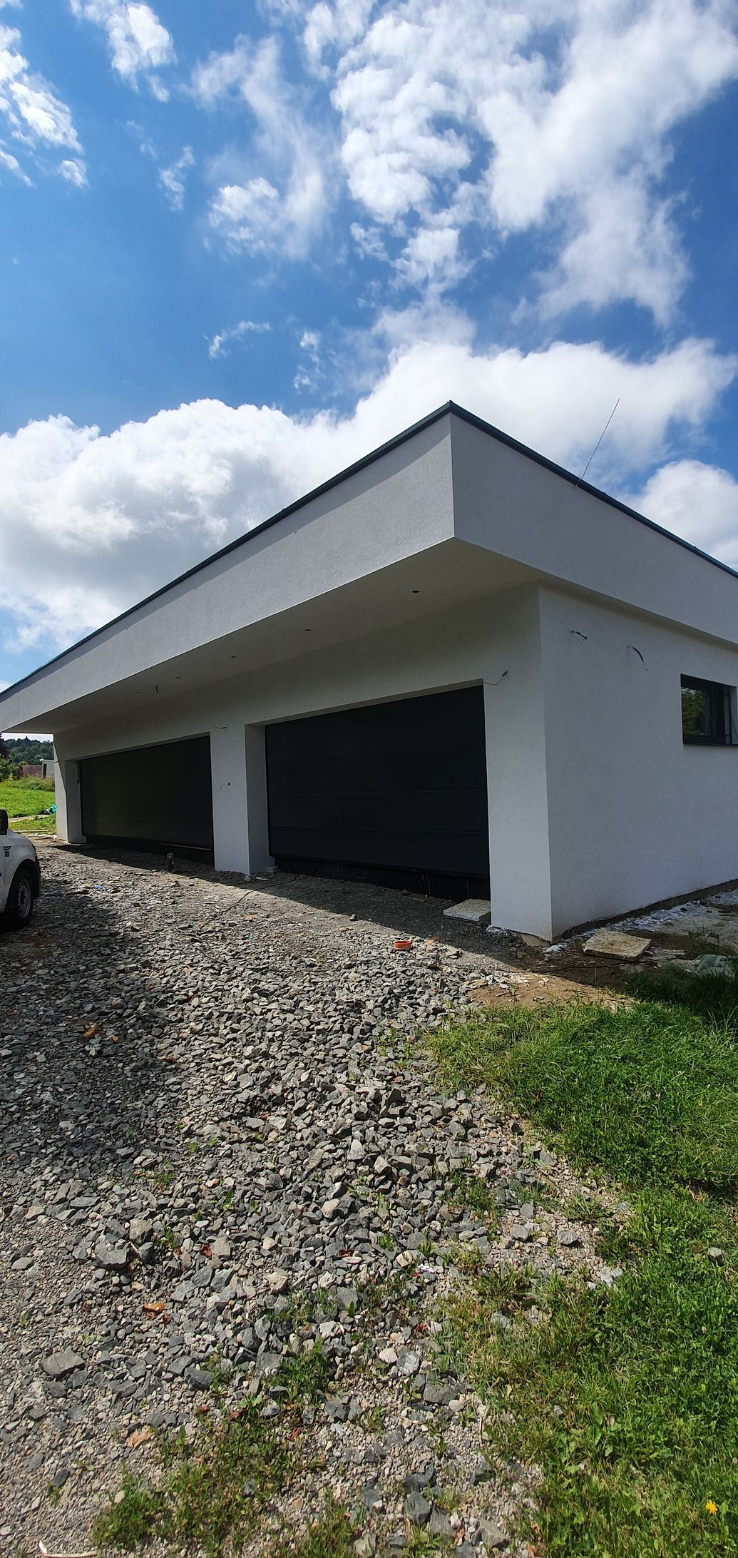 Weißes Gebäude mit zwei geschlossenen Garagentoren, Kiesauffahrt und blauem Himmel.