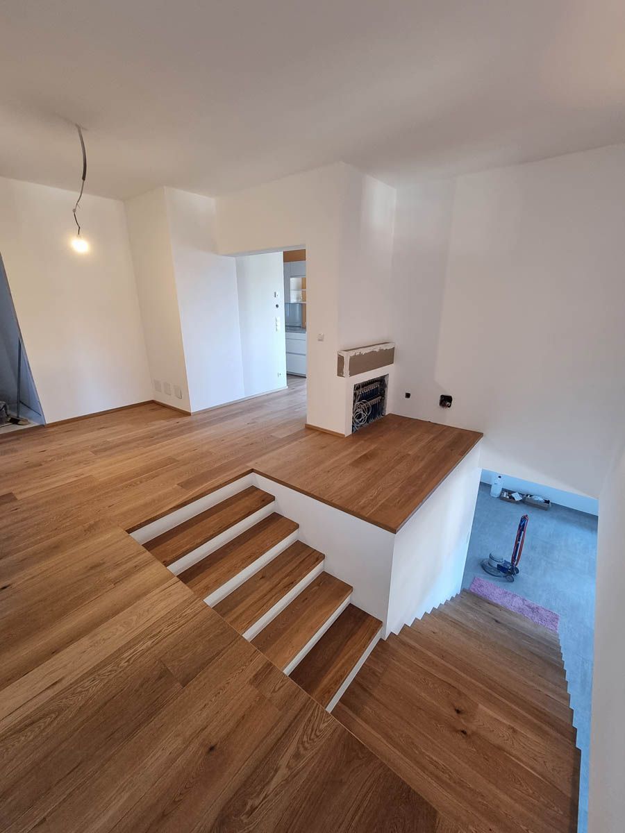 Holztreppe, die zu einer erhöhten Plattform mit Kamin und lichtdurchflutetem Innenraum führt.