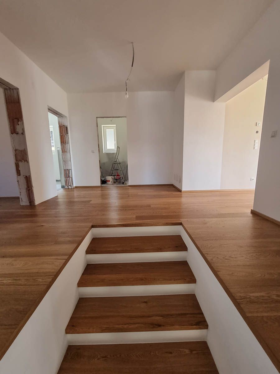 Eine Holztreppe führt in einen hellen, leeren Raum mit Holzböden und weißen Wänden.