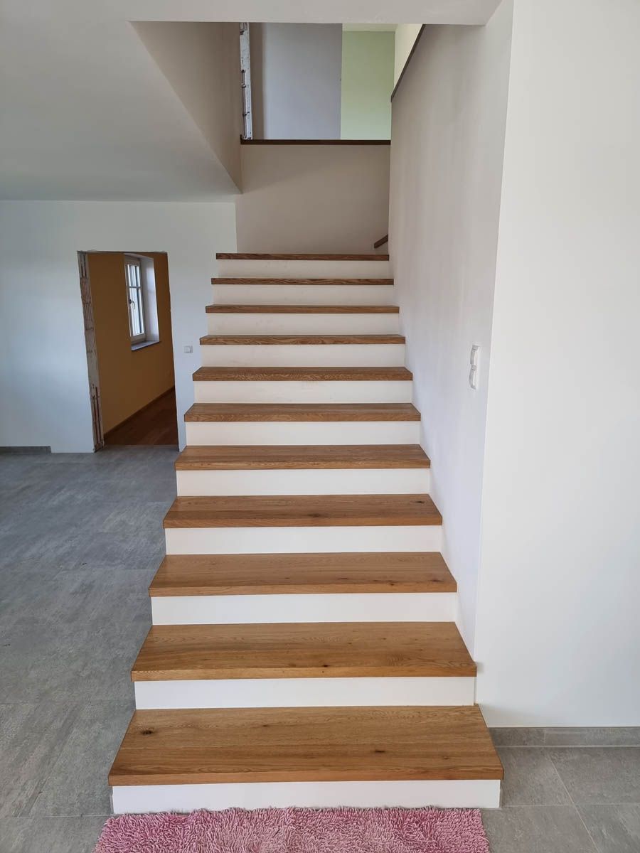Holztreppe mit weißen Setzstufen, die in den zweiten Stock führt.