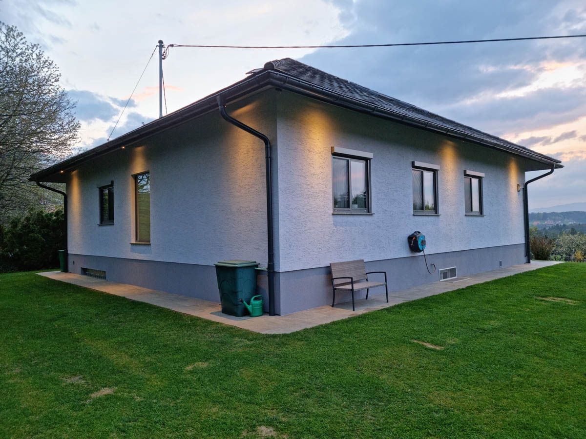 Ein modernes Haus mit grauen Wänden, schwarzen Zierleisten und einem dunklen Dach in der Abenddämmerung; Rasen im Vordergrund.
