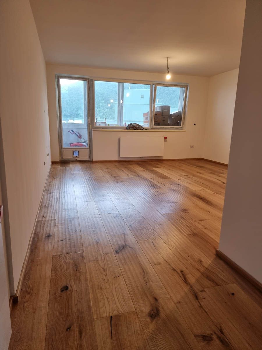 Leerer Raum mit Holzboden, einem Fenster und Beleuchtungskörpern.