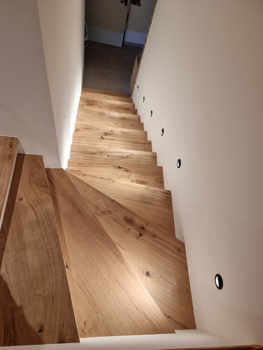 Holztreppe mit eingebauten Lichtern an den Stufen und der Wand, die zu einem Flur hinunterführt.