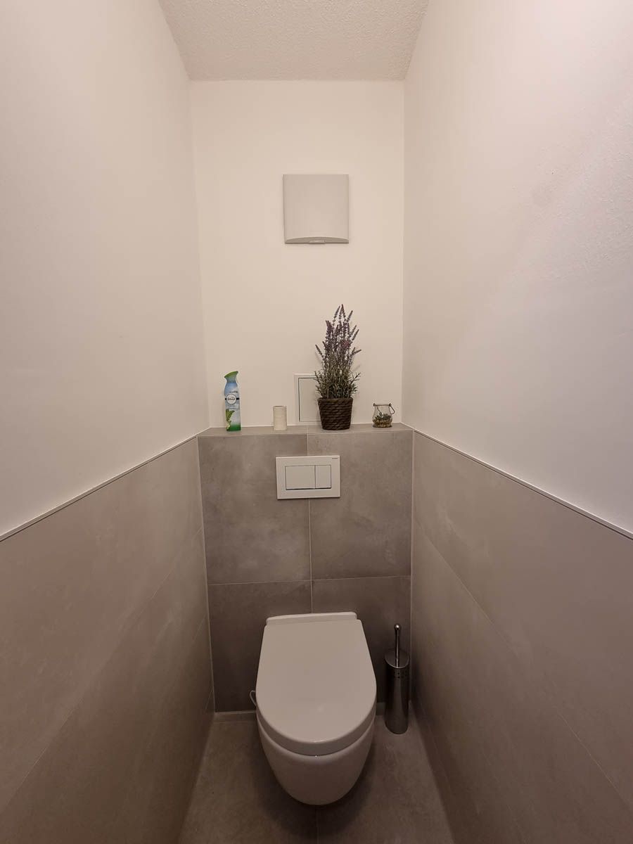 Kleiner, moderner Toilettenraum mit grauen und weißen Wänden, einer Toilette und Dekorationsgegenständen.