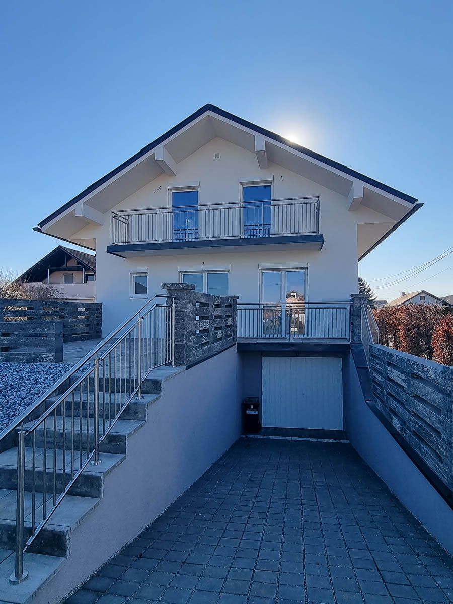 Zweistöckiges weißes Haus mit Garage, Balkon und Treppe. Geländer aus Edelstahl und blauer Himmel.
