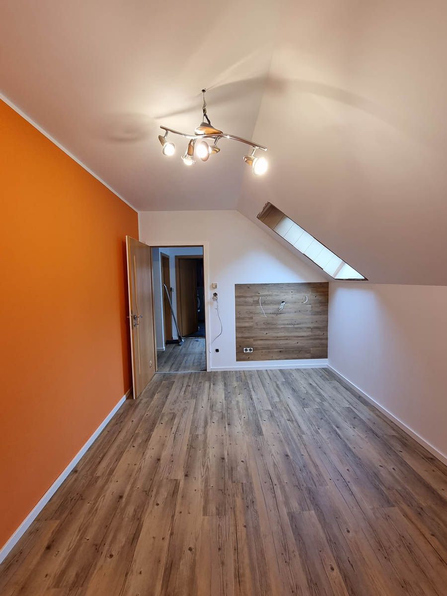 Leerer Dachbodenraum mit Holzboden, orangefarbener Wand und einem hölzernen Wandelement.