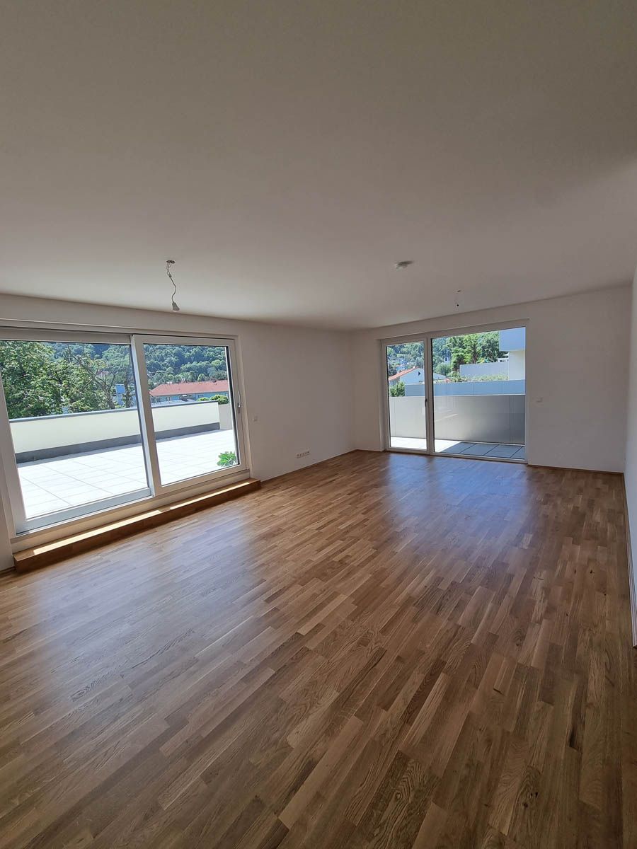 Leerer Raum mit Hartholzboden, großen Fenstern und Zugang zu einem Balkon.