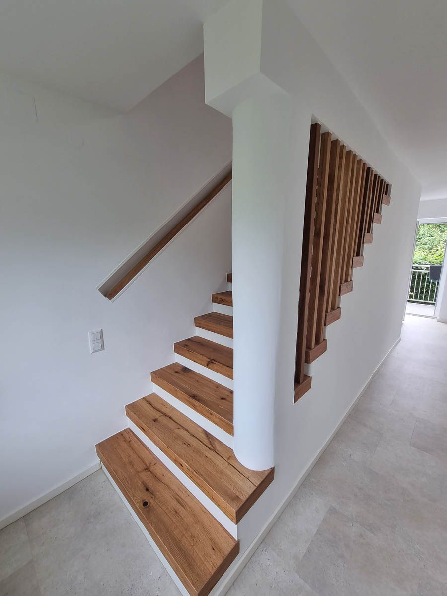 Holztreppe mit weißer Wand, Handlauf und dekorativer Holzplatte.