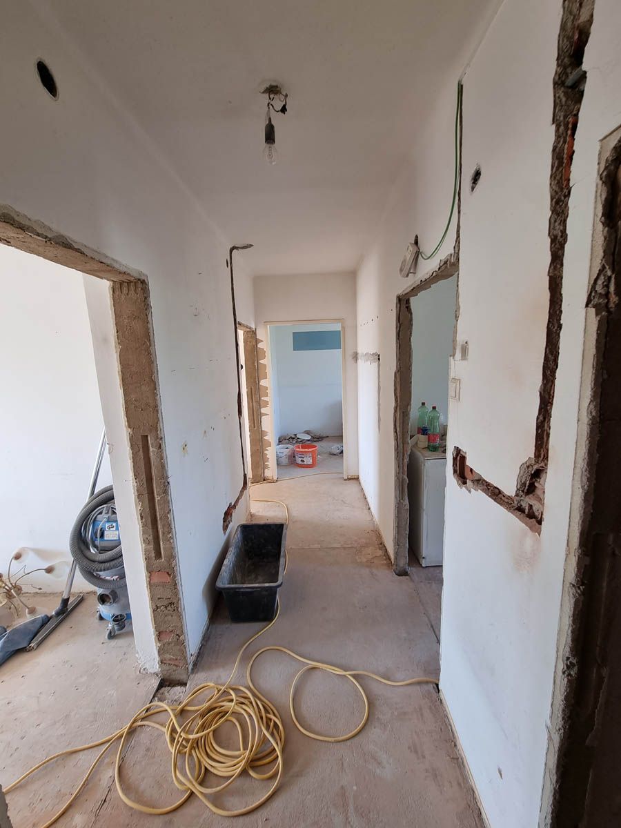 Flur im Bau, mit offenen Türen und freiliegenden Leitungen, vom Eingang aus gesehen.