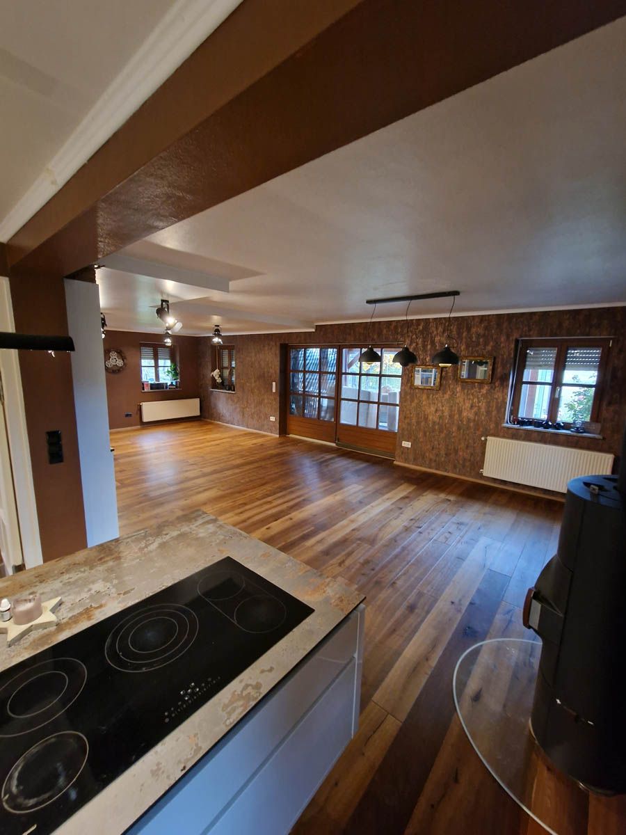 Offener Küchen- und Wohnbereich mit Holzboden, braunen Wänden und einem schwarzen Herd.