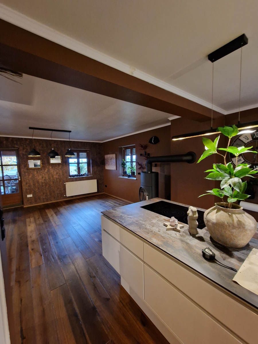 Geräumige Küche mit Holzböden, braunen Wänden und einer modernen Kochinsel. Auf der Arbeitsplatte steht eine Pflanze.