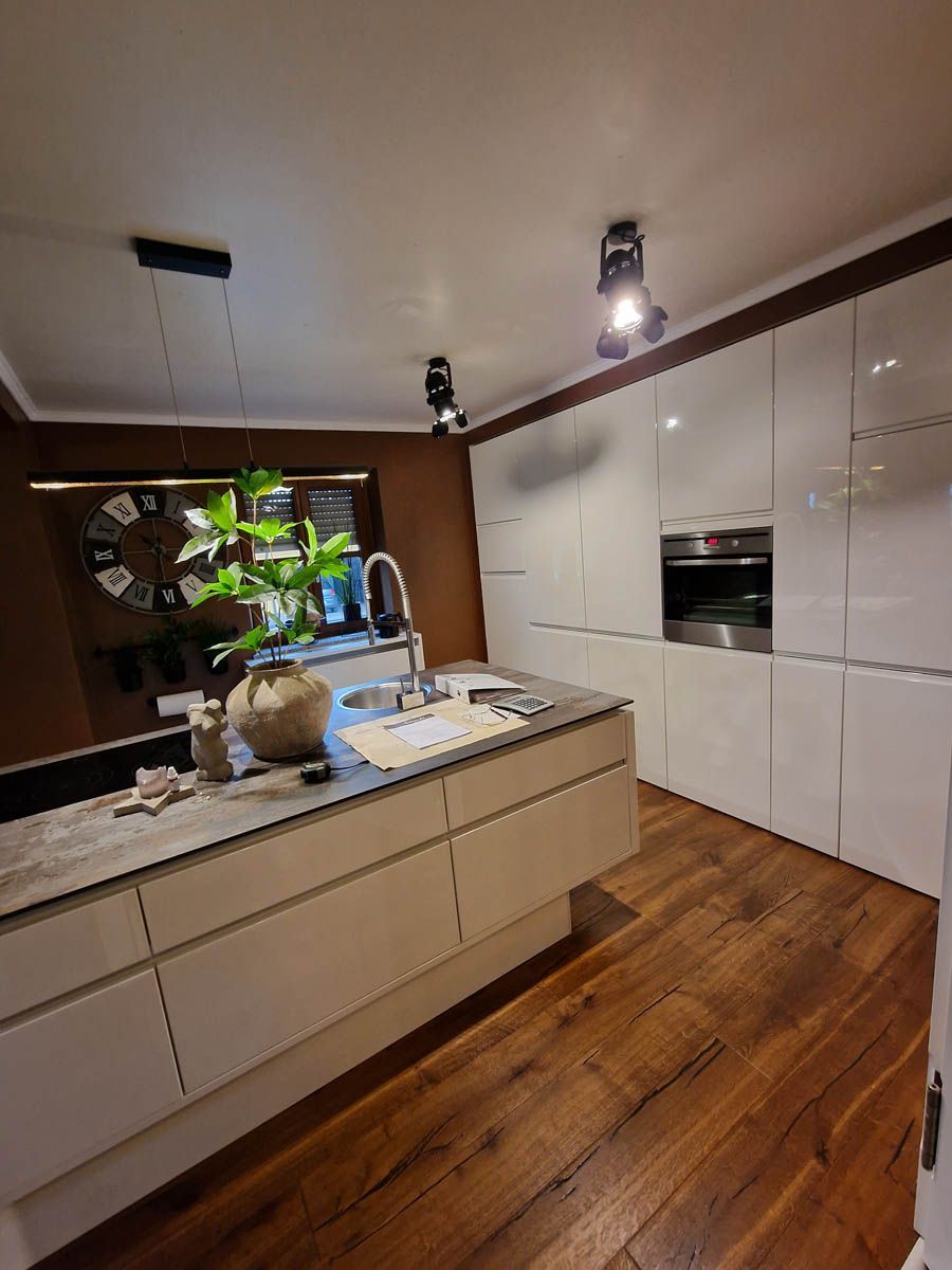 Moderne Küche mit weißen Schränken, Holzböden und Kochinsel. Braune Wand mit Uhr und Spüle.
