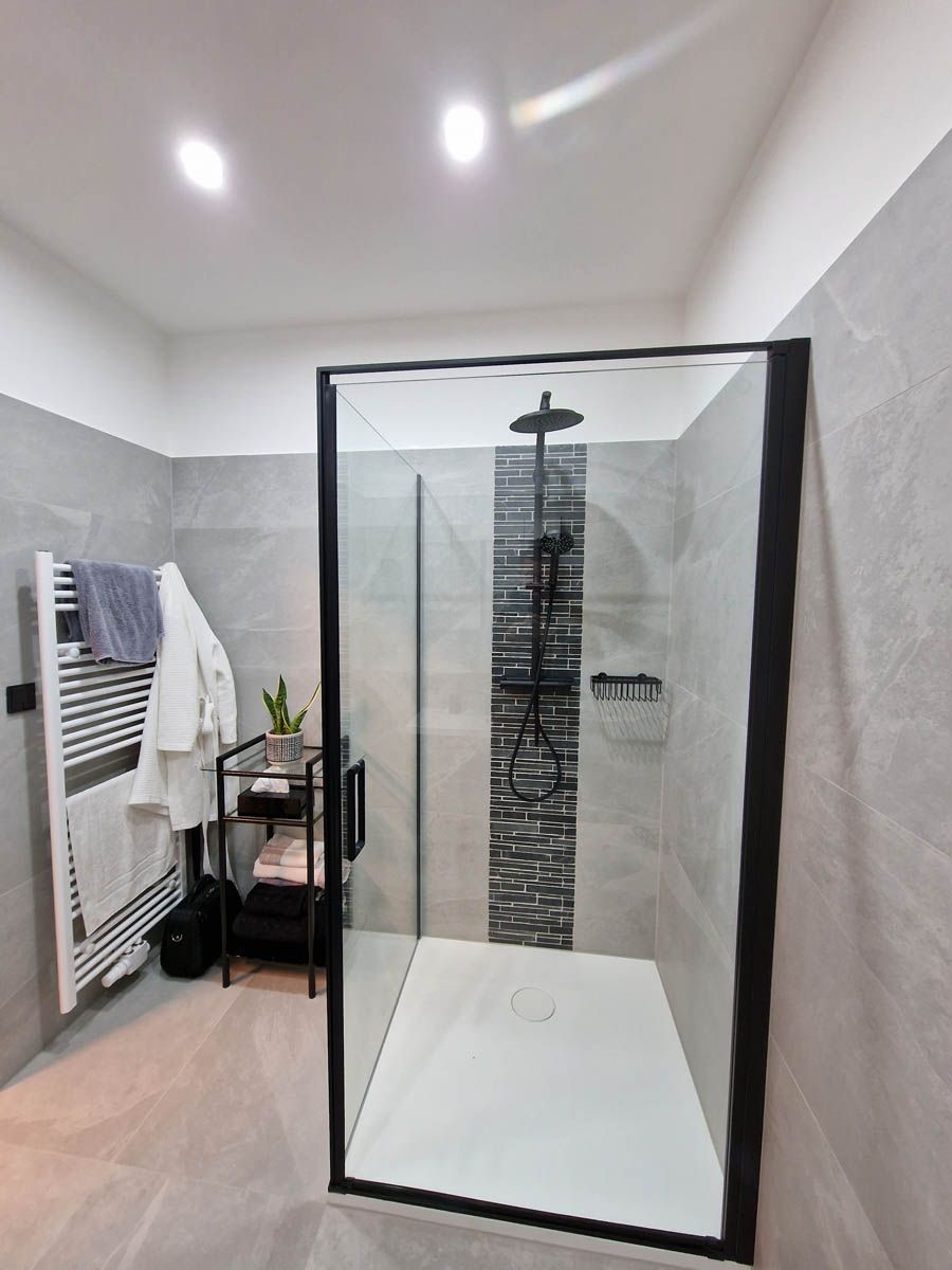 Modernes Badezimmer mit ebenerdiger Dusche, grauen Fliesen, schwarzem Duschrahmen und Handtuchhalter.