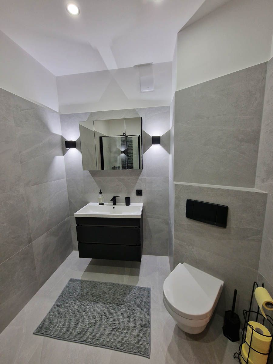 Modernes graues Badezimmer mit schwebendem Waschtisch, Toilette und Wandleuchten.