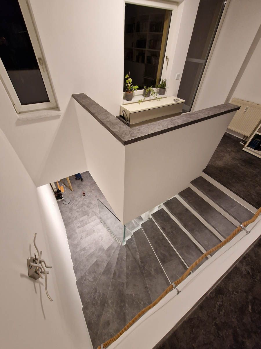 Innenansicht einer modernen Treppe mit grauen Stufen und weißen Wänden. Pflanzen stehen auf einem Fensterbrett.