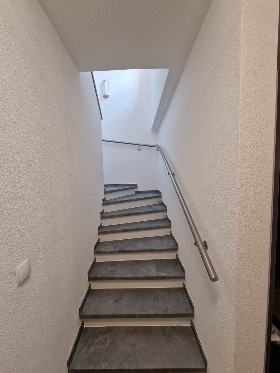 Treppe mit Betonstufen und Metallhandlauf nach oben, weiße Wände.
