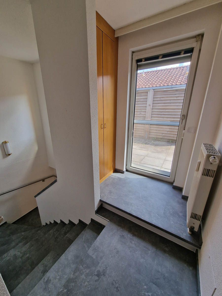 Ein Treppenabsatz mit einer Tür zu einem Außenbereich und einem Holzschrank. Graue Stufen und Wände.