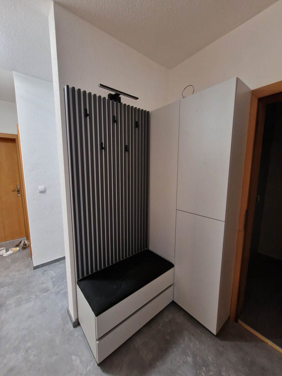 Flur mit weißem Lagerschrank, Bank, dunkler strukturierter Wand und Kleiderhaken.