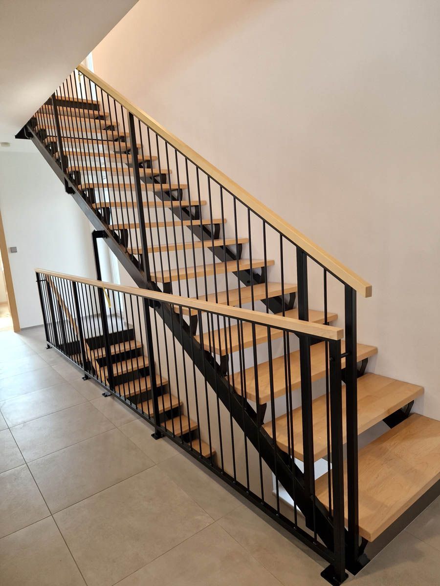 Holztreppe mit schwarzem Metallgeländer, hellen Holzstufen und einer weißen Wand.