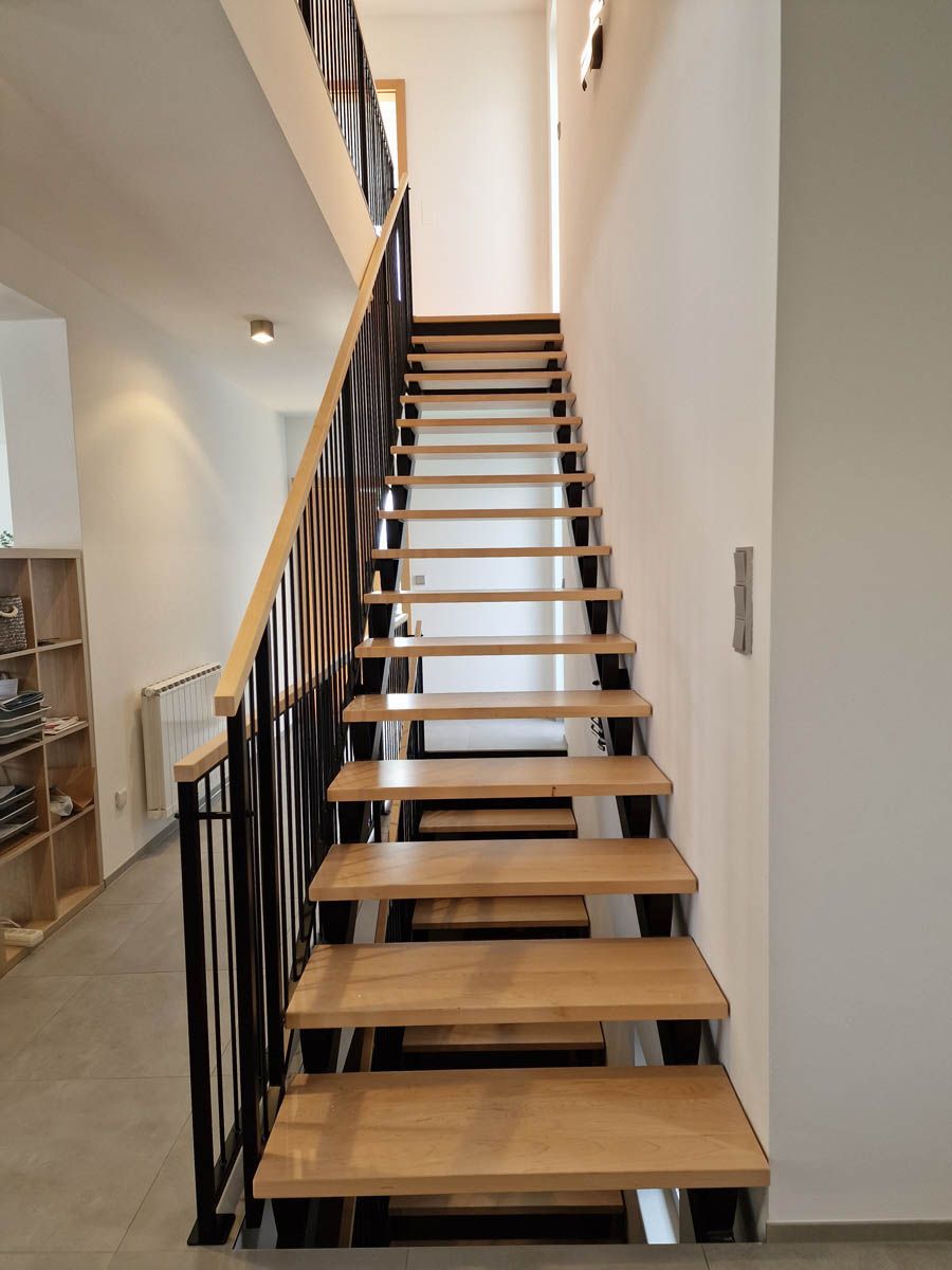 Holztreppe mit schwarzem Metallgeländer, weiße Wände.