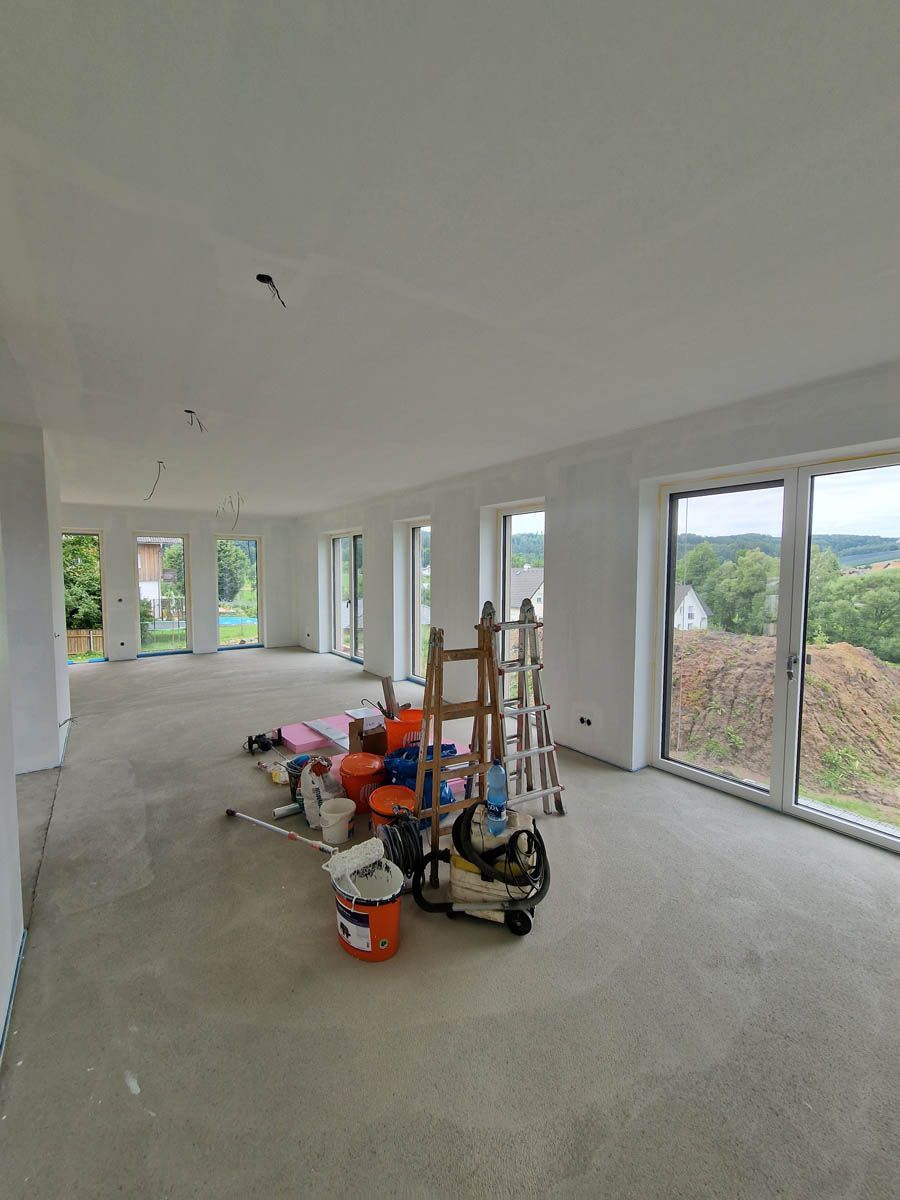 Leerer Raum im Bau mit weißen Wänden, Fenstern und verstreuten Werkzeugen.