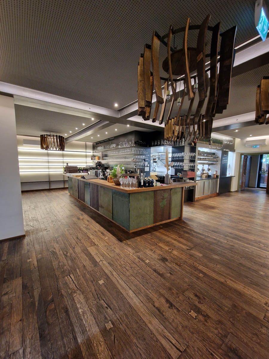 Restaurant-Innenraum mit Holzböden, rustikaler Bar und dekorativer Hängekunst.