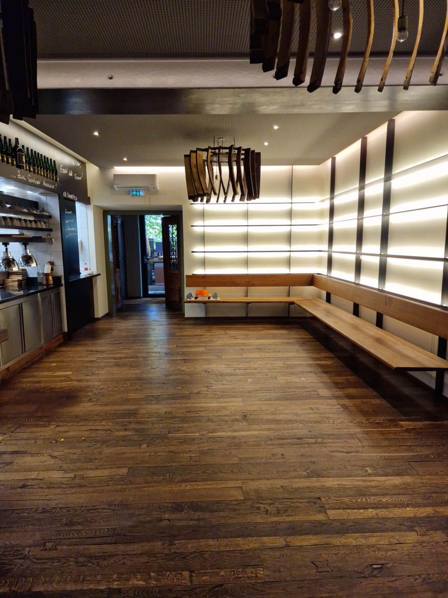Innenansicht eines Restaurants mit Holzböden, einer langen Bank und einer dekorativen Leuchte.
