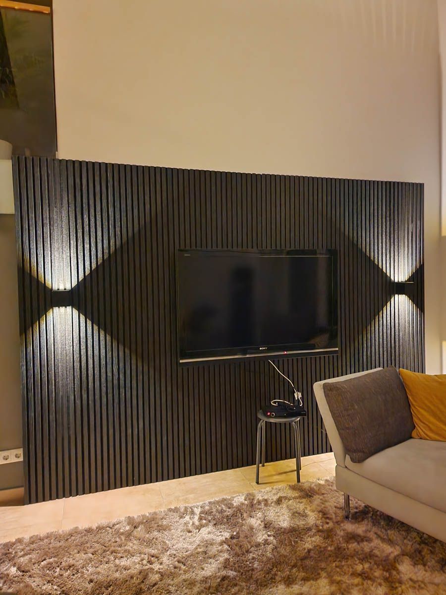 Schwarze strukturierte Wand mit montiertem Fernseher, Wandleuchten und einem Sofa.