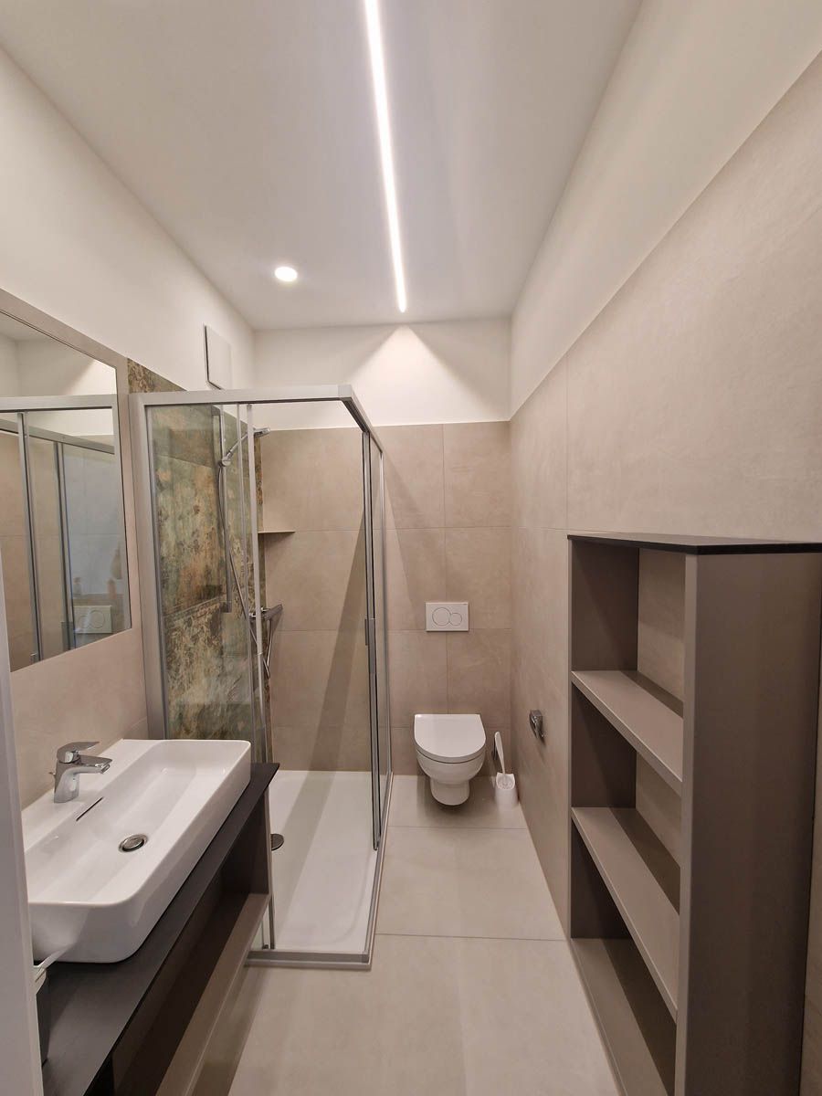 Modernes Badezimmer mit Dusche, Toilette, Waschbecken und Regalen in neutralen Tönen.