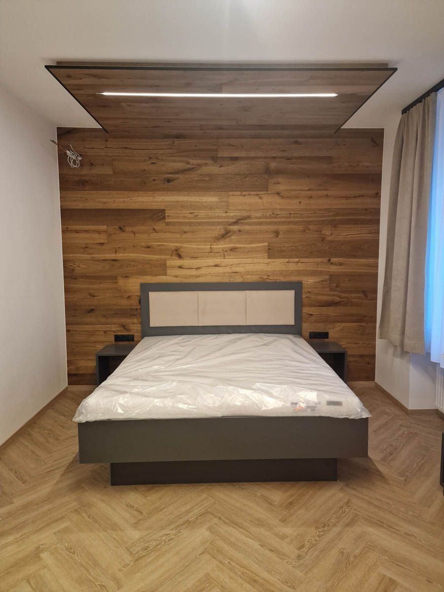 Schlafzimmer mit Akzentwand aus Holz, Bett, Nachttischen und gemustertem Holzboden.