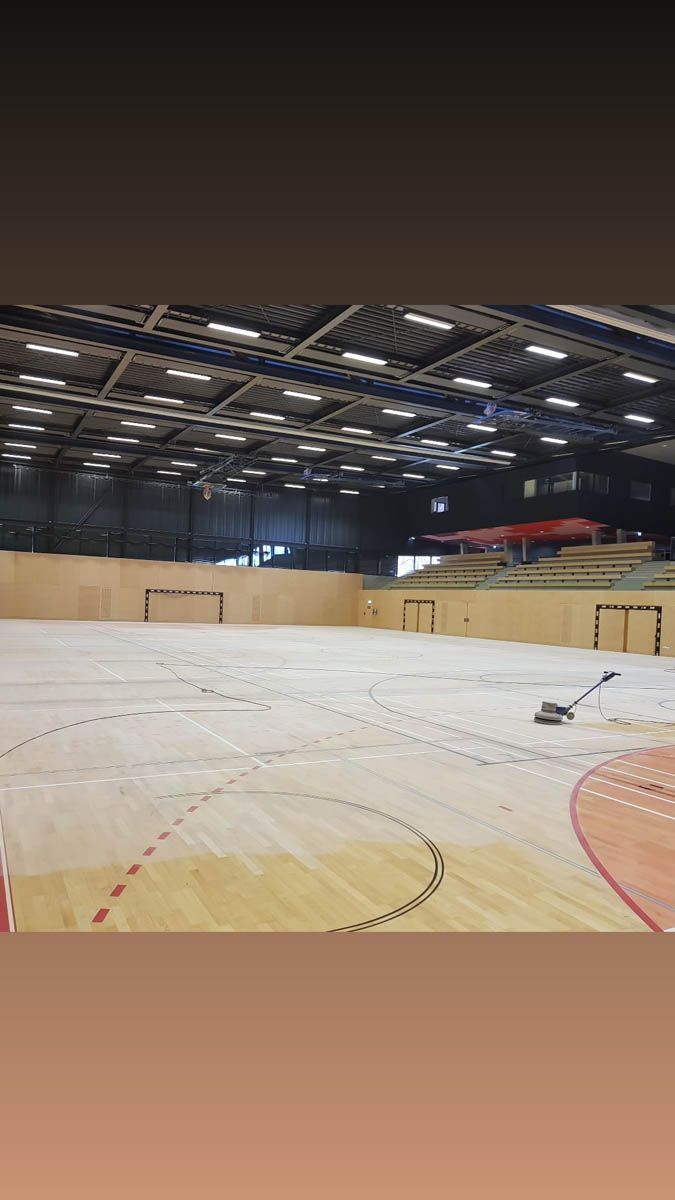 Leere Sporthalle mit Holzboden und Tribüne.
