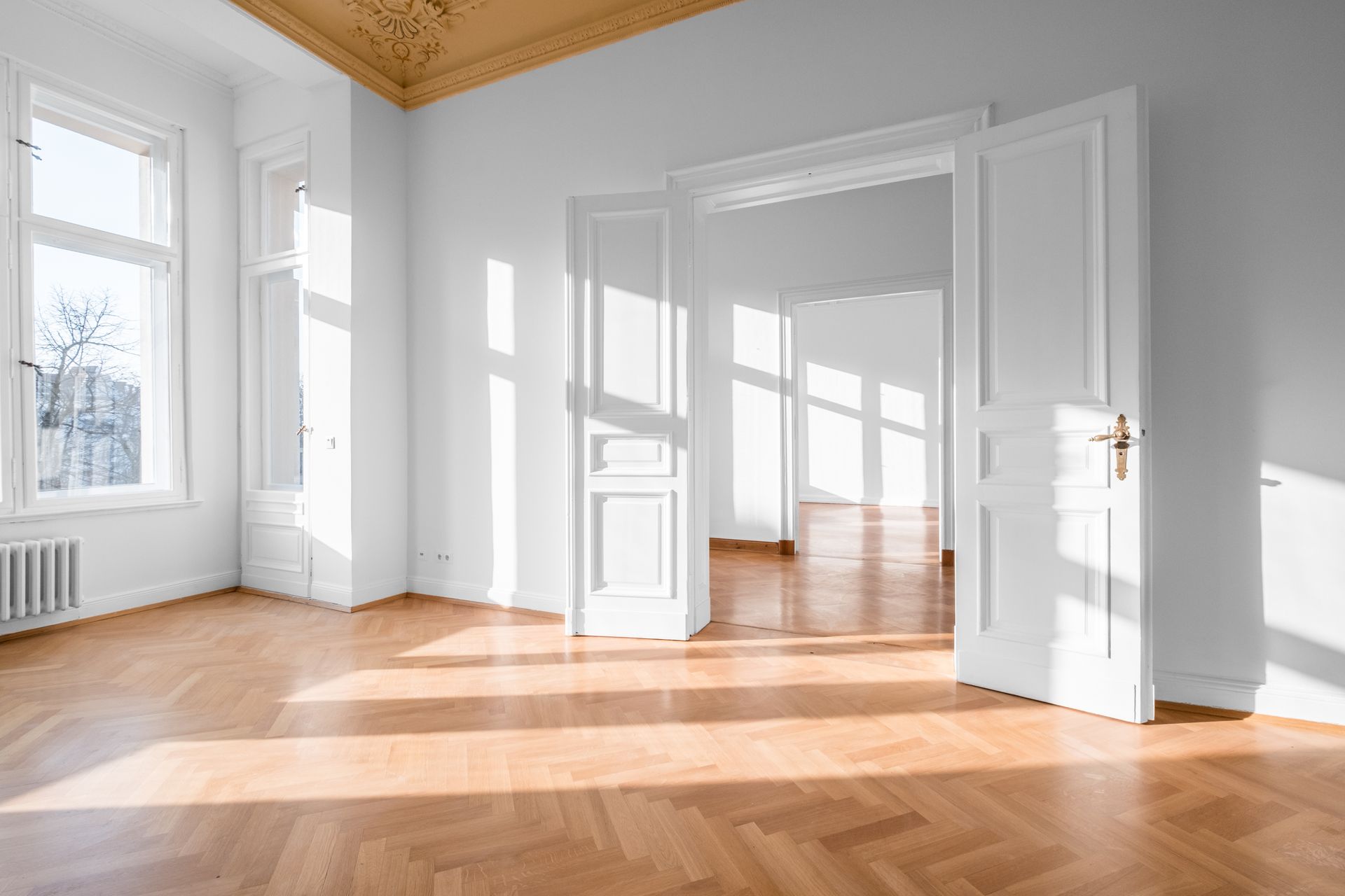 Heller, leerer Raum mit Hartholzböden, weißen Wänden und offenen Türen; Sonnenlicht strömt durch die Fenster herein.