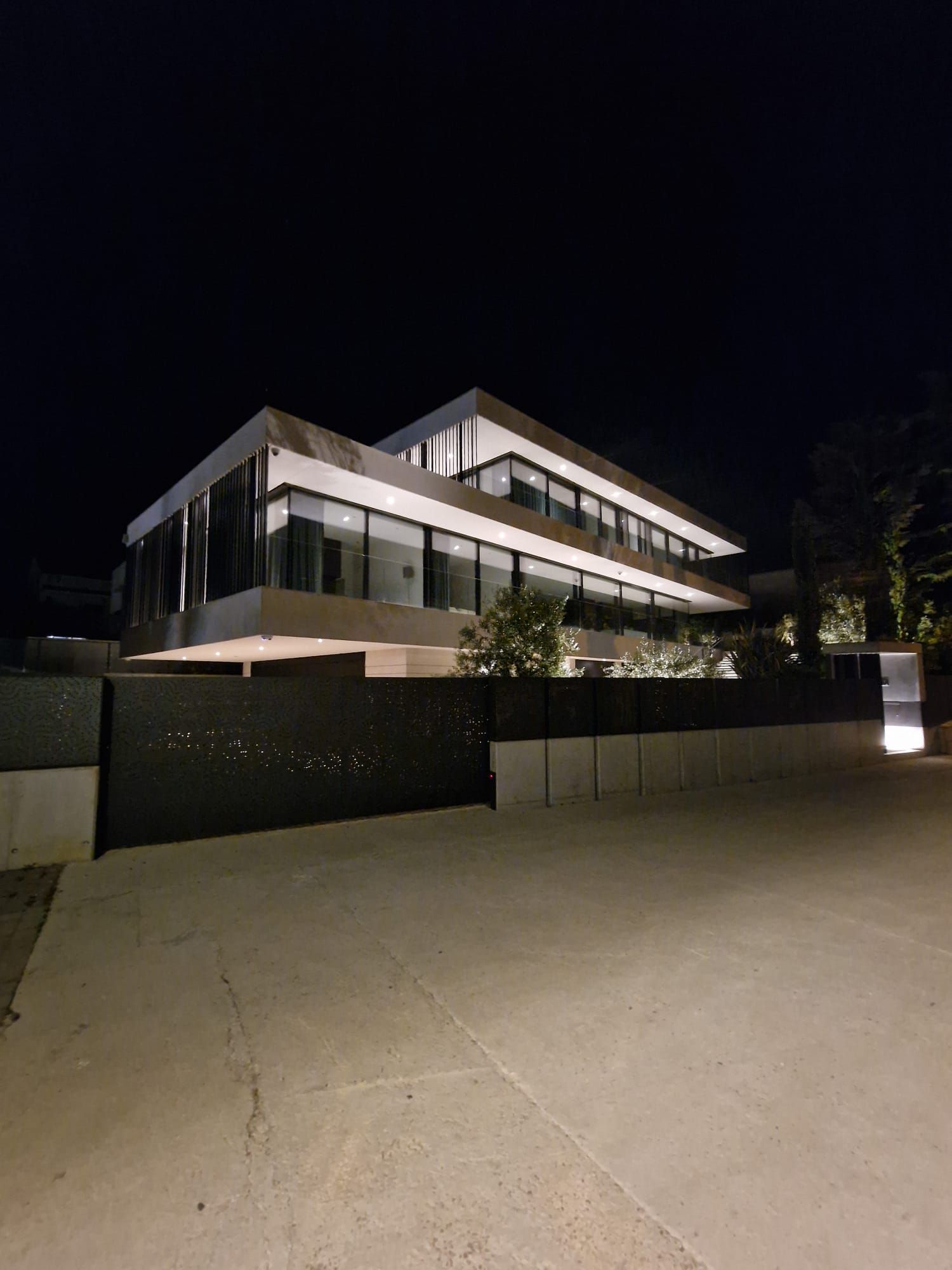 Modernes, zweistöckiges Haus bei Nacht mit großen Fenstern und einem schwarzen Tor.