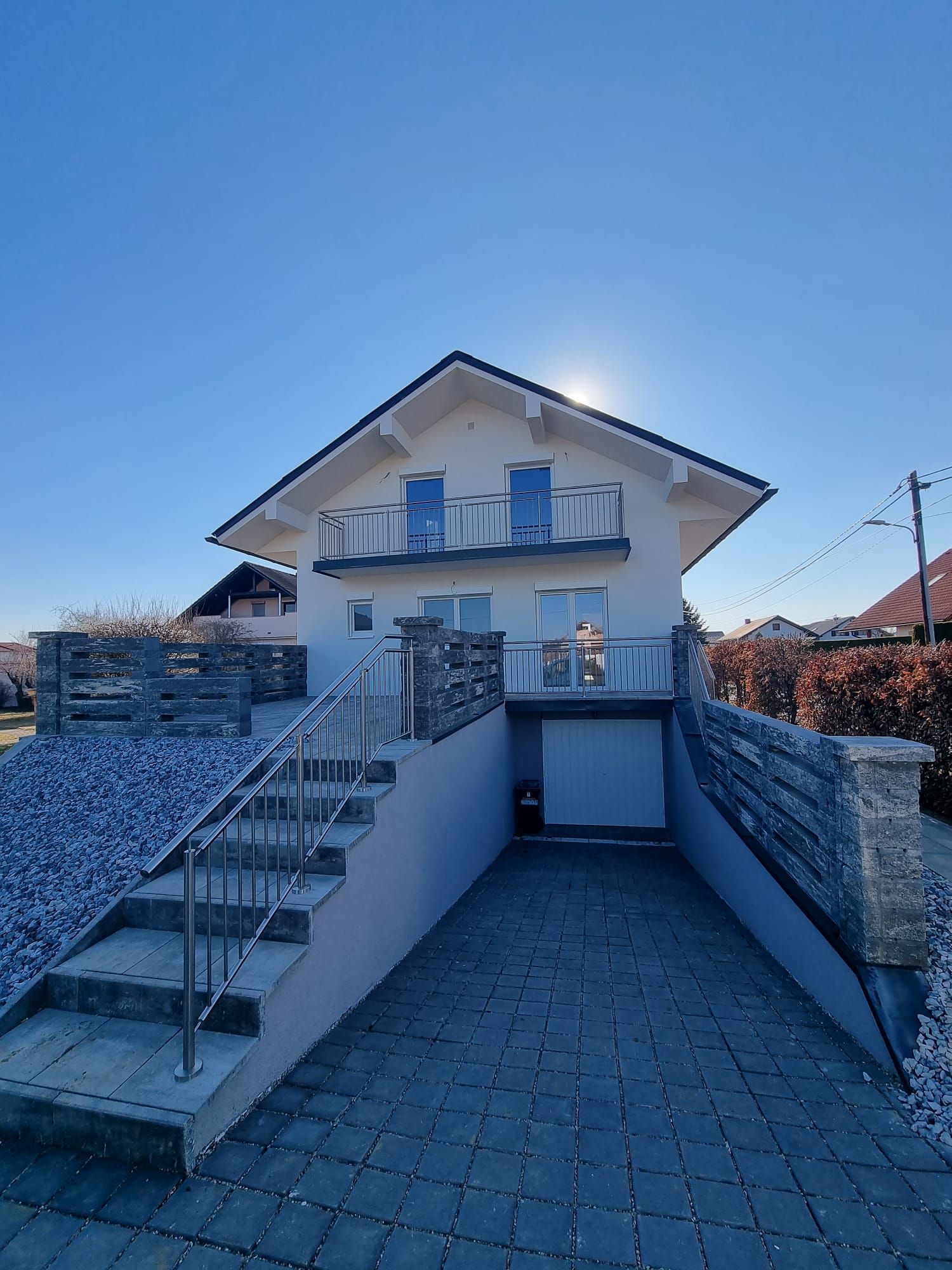 Weißes Haus mit Balkon, Garage und Stufen, die an einem sonnigen Tag zum Eingang führen.