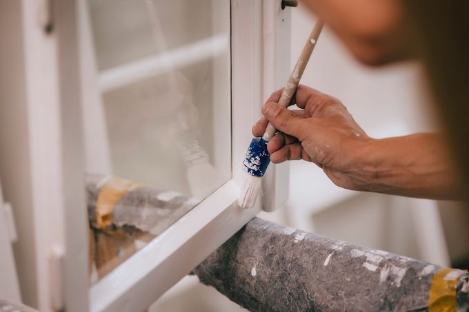 Person, die einen weißen Fensterrahmen mit einem Pinsel bemalt.