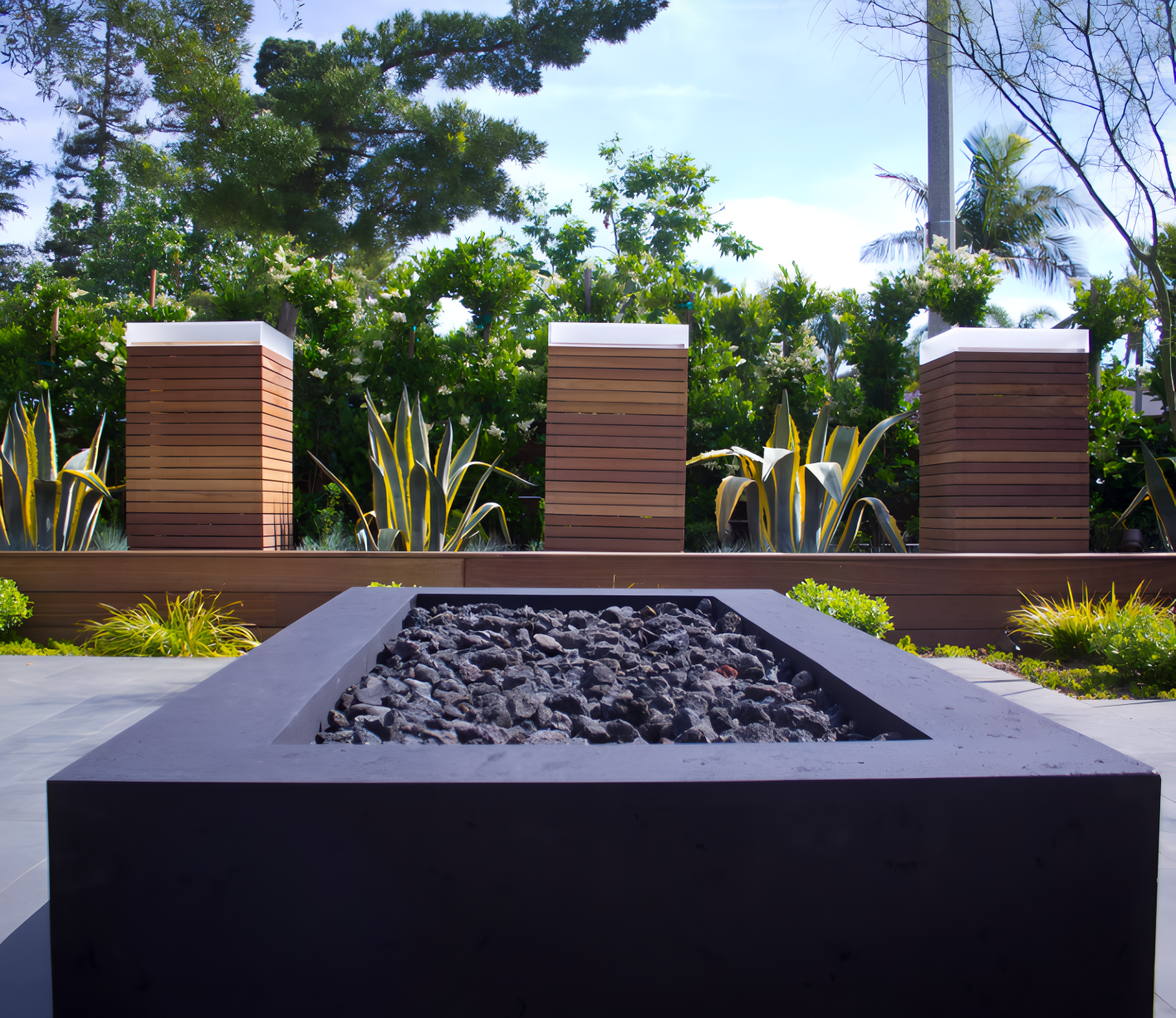 Modern fire pit with dark stones, wood accents, and landscaping.