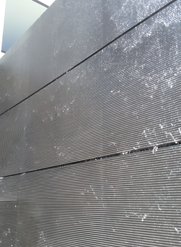 Close-up view of a textured, dark gray wall with horizontal and curved lines, possibly a water feature.