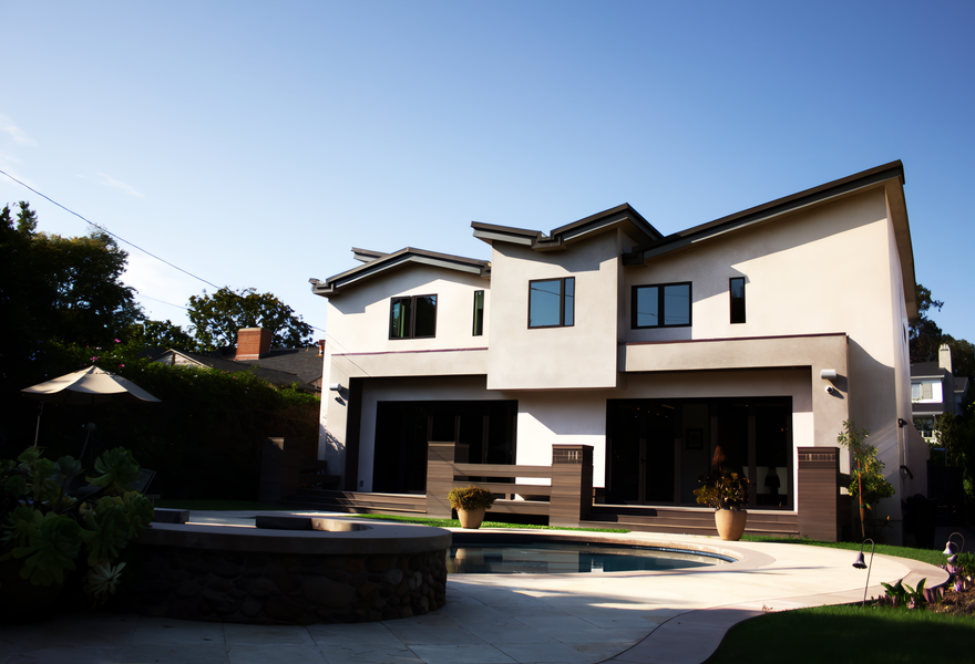 Modern two-story house with pool, patio, and greenery. Beige stucco, dark windows, and a sunny day.