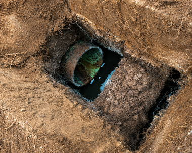 Aerial view of a rectangular dirt excavation with two green pipes or tanks exposed in the center
