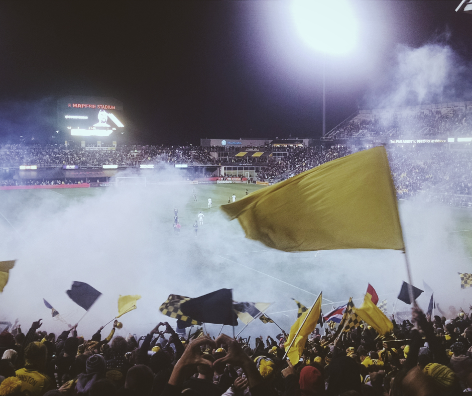 soccer stadium with fans waving their teams flag and throwing smoke.