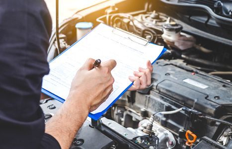 a mechanic is writing on a clipboard while working on a car .