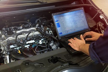 a mechanic is using a laptop computer to check the engine of a car .