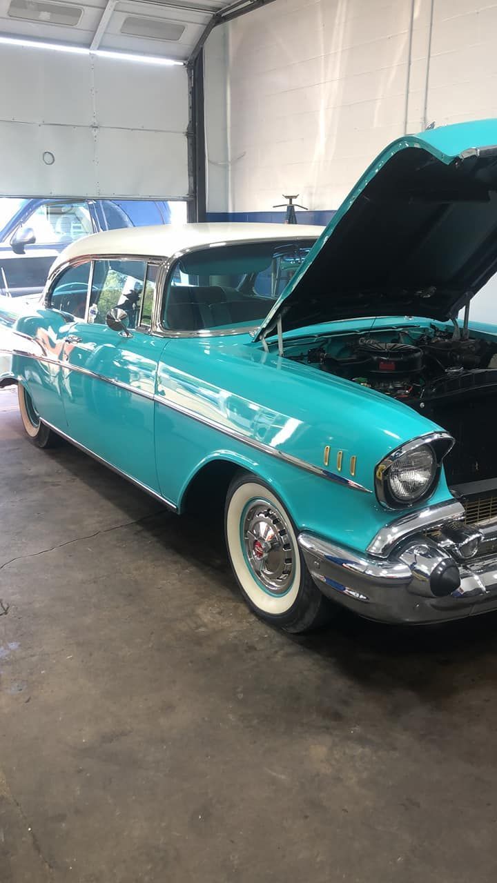 A blue and white car with the hood open is parked in a garage.