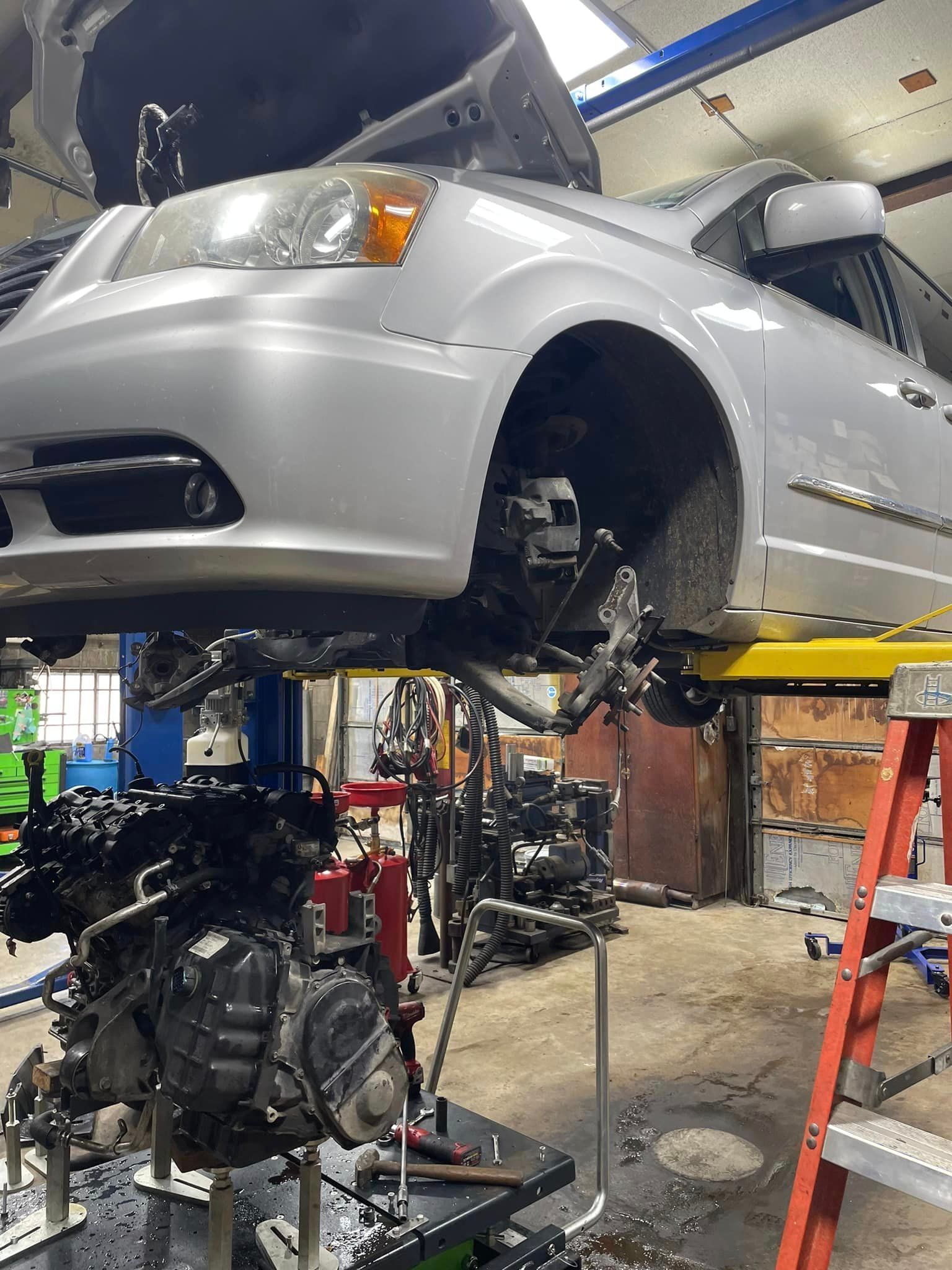 A car is being repaired in a garage with the hood up.